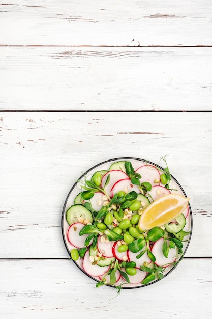 Foto insalata fresca con ravanello cetriolo pisello verde girasole soia e germogli di fagioli mung edamame e semi di lino vegetariano vegano cibo sano vista dall'alto vecchio tavolo da cucina bianco