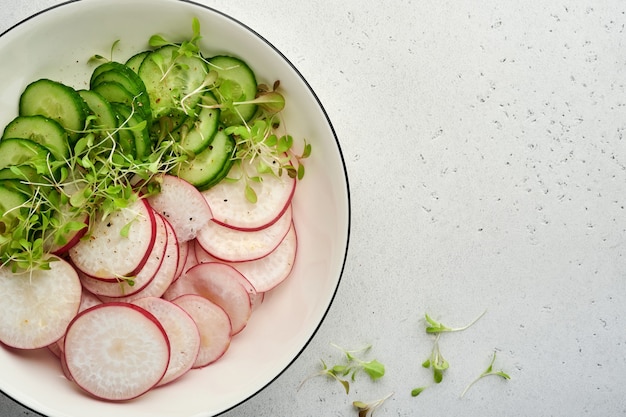 fresh salad with red radish, cucumber, vegetables, microgreen radishes in white plate