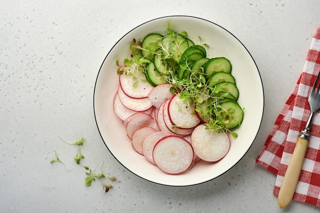 свежий салат с красной редькой, огурцом, овощами, микрозелеными редисами в белой тарелке