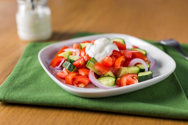 Fresh salad with tomato, cucumber and onion, seasoned with sour cream