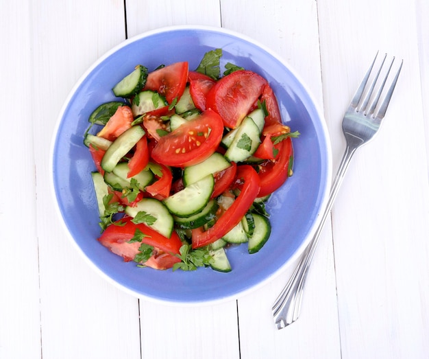 Fresh salad with tomatoes and cucumbers on white wooden background