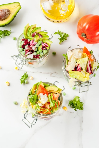 Fresh salads in jar with fresh vegetables and healthy dressings,  on white marble table, 