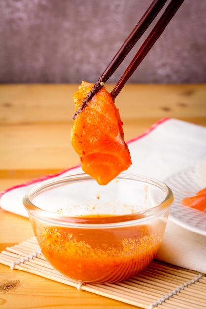 Fresh salmon being picked up from a seafood sauce bowl with a wooden chopstick