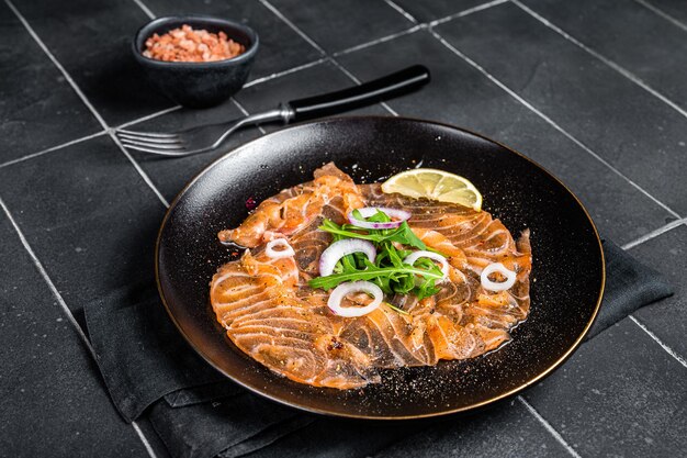 Fresh Salmon carpaccio with onion and arugula on a plate Black background Top view