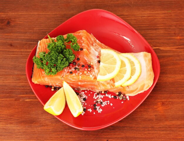 Fresh salmon fillet with herbals and lemon slices on plateon wooden background