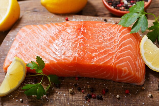 Fresh salmon fillet with ingredients for cooking on a wooden board, top view