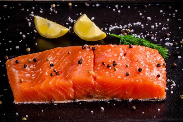 Fresh salmon fillet with lemon pepper and sea salt on dark background