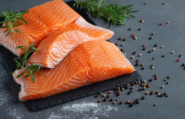 Fresh salmon fillets on black cutting board with herbs and spice on a grey background