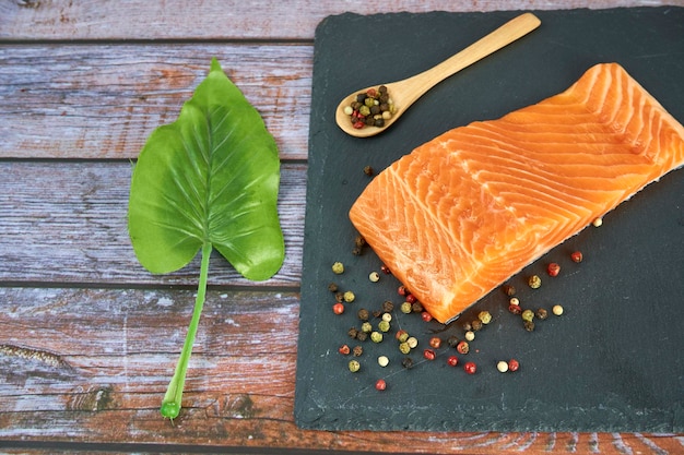 Fresh salmon fillets on black cutting board with herbs and spice