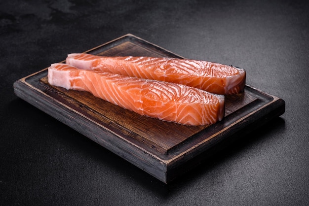 Fresh salmon fillets on black cutting board with herbs and spices