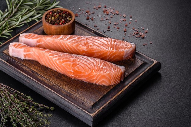 Fresh salmon fillets on black cutting board with herbs and spices