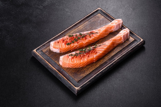 Fresh salmon fillets on black cutting board with herbs and spices