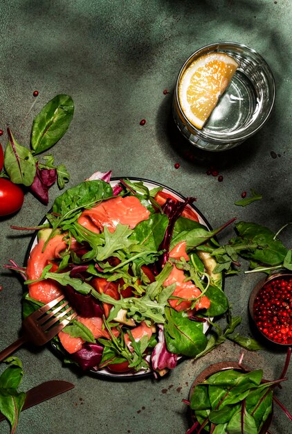 Insalata di salmone fresco con foglie di barbabietola pomodori radicchio limone e olio d'oliva condimento per cheto e dieta a basso contenuto di carboidrati sfondo verde arrugginito luce dura vista dall'alto spazio di copia