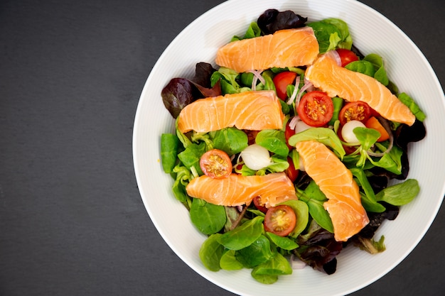 Fresh salmon salad with sweet tomatoes, pickled garlic, onions and spinach are a healthy diet for every meal.