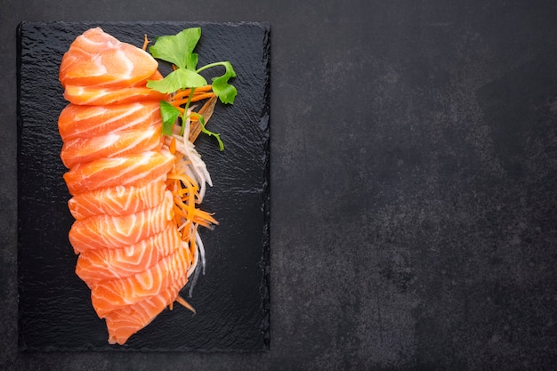 fresh salmon sashimi fillet with carrot, radish slice and celery in black slate