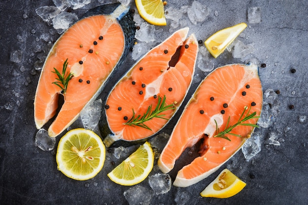 Fresh salmon steak with herbs and spices lemon rosemary on black plate background / Raw salmon fish fillet and ice for cooked steak seafood