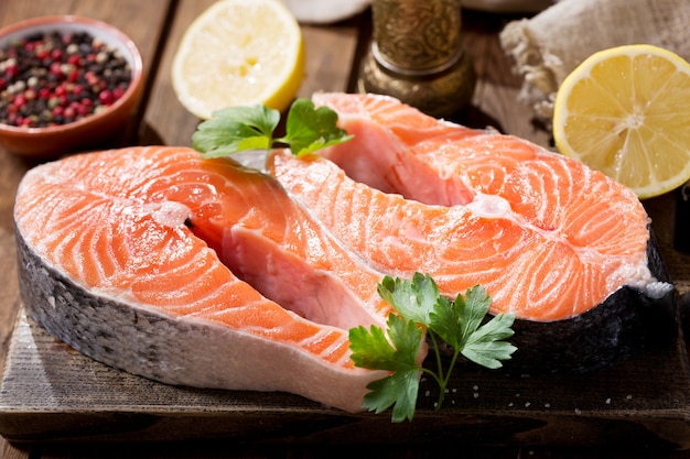 Fresh salmon steaks with ingredients for cooking on a wooden table