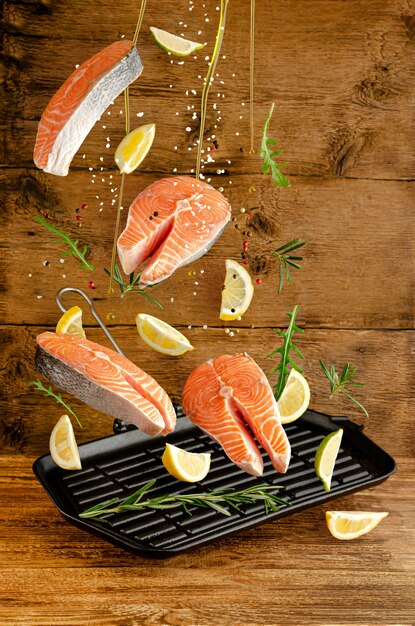 Fresh salmon or trout fish with spices and herbs falling on grill pan on wooden background. Flying food and levitation concept.