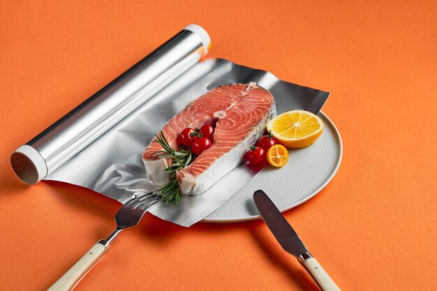 Fresh salmon with lemon in foil paper, ready for cooking in oven on orange background.