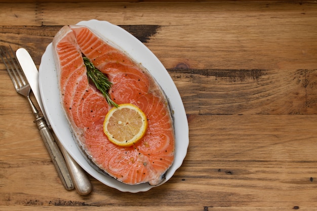 Fresh salmon with lemon on white dish on brown wooden surface