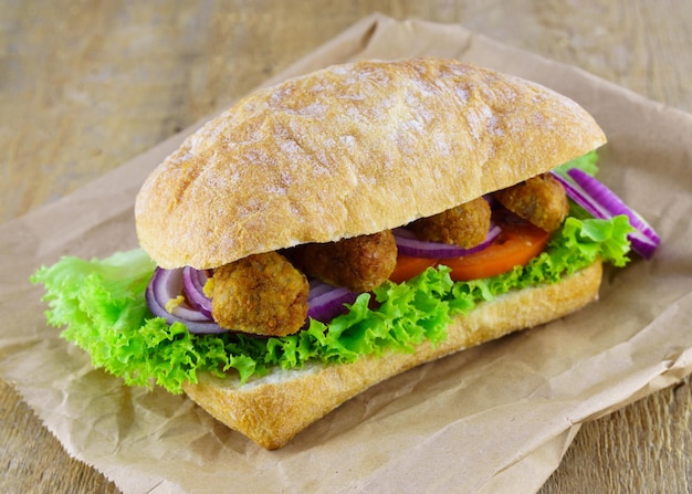 Fresh sandwich bread ciabatta onion, tomatoes, lettuce, beans cutlets on rough rustic wooden table background.