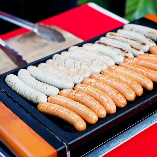 Fresh sausage and hot dogs grilling outdoors on a gas barbecue grill.