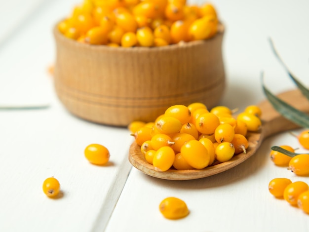Fresh sea buckthorn berries in a wooden bowl and spoon against the background of leaves and branches with berries