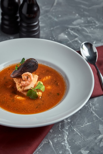 Fresh seafood soup in a white plate on dark background, side view