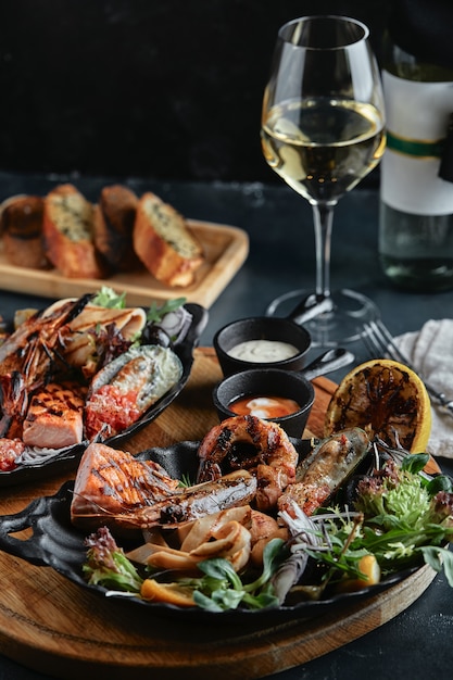 Fresh seafood and white wine on a stone table. Oysters, prawns and scallops, squids, served by the chef, beautifully laid out on plates, dark concrete space.