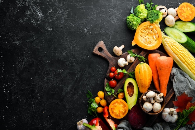 Fresh seasonal vegetables on a black stone background Pumpkin tomato avocado cucumber onion carrot Autumn food Top view Free copy space