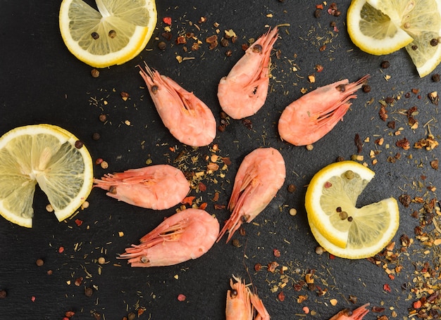 Fresh shrimp and lemon slices on black board, top view