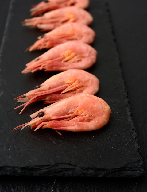 Fresh shrimp in a row on a black slate board, close up