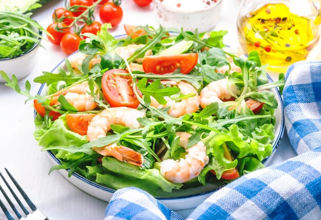 トマトレタスルッコラアボカドキュウリとレモンドレッシングと白い背景の新鮮なエビのサラダ健康的な食事きれいな食品のコンセプト上面図
