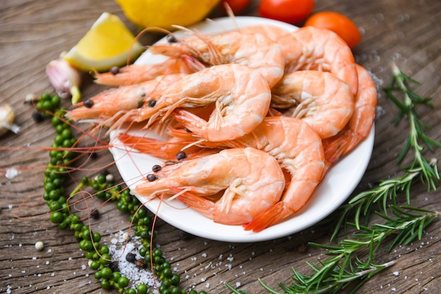 Fresh shrimp on white plate with ingredients herb and spices / cooking seafood shrimps prawns served on a wooden table