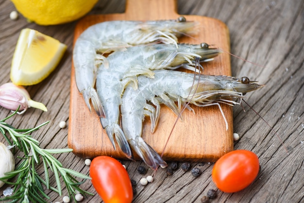 Fresh shrimp on wooden cutting board with ingredients herb and spices for cooking seafood - raw shrimps prawns