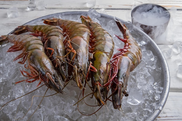 Fresh shrimps on ice cubes. Plate with raw prawns. Exotic food bought at supermarket. Dry ice in a bowl.