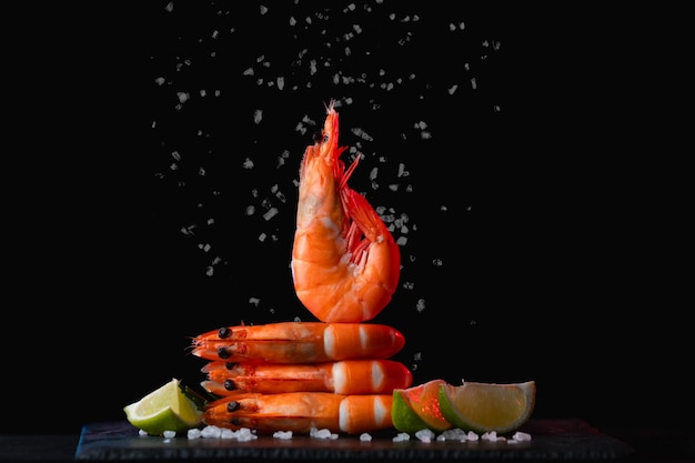 Photo fresh shrimps with lime and rosemary and salt on black background closeup