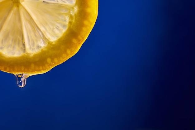 Fresh slice of lemon juice drip on blue background citrus dripping isolated copy space