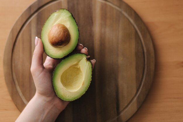 Fresh sliced avocado in woman's hand on green plate. Vegetarian food concept.