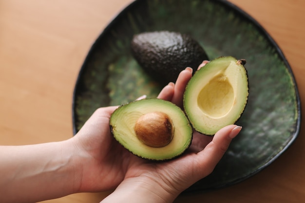 Fresh sliced avocado in woman's hand on green plate. Vegetarian food concept.