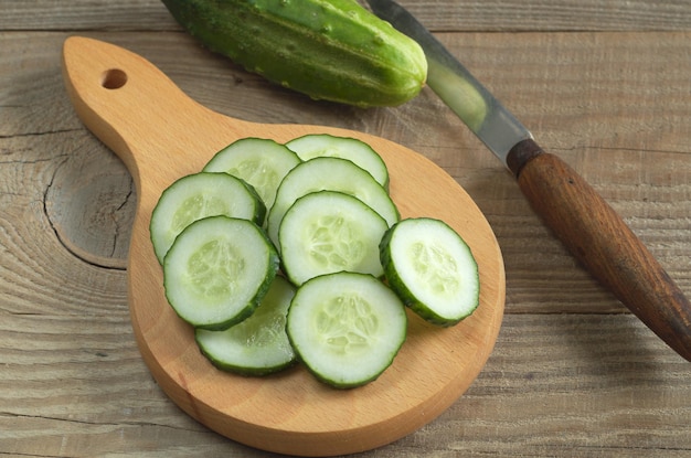 Fresh sliced cucumber and knife on wooden cutting board