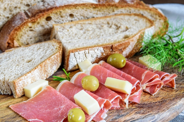 Primo piano affettato fresco di serrano del jamon. pane integrale fatto in casa, formaggio e olive per merenda sul legno.