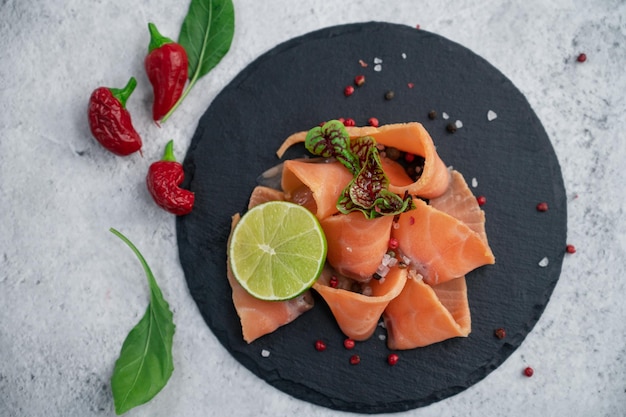 Fresh smoked salmon slices with peppers greens and lime on concrete background