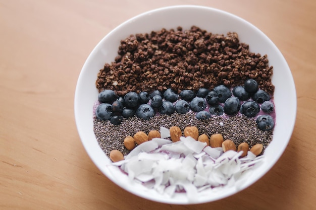 Fresh smoothie bowl with blueberry chia seeds almonds coconut flakes and chocolate flakes Morning breakfast on wooden table Lactose free yogurt