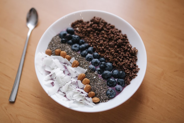 Frullato fresco ciotola con mirtilli, semi di chia, mandorle, scaglie di cocco e scaglie di cioccolato. colazione mattutina sulla tavola di legno.