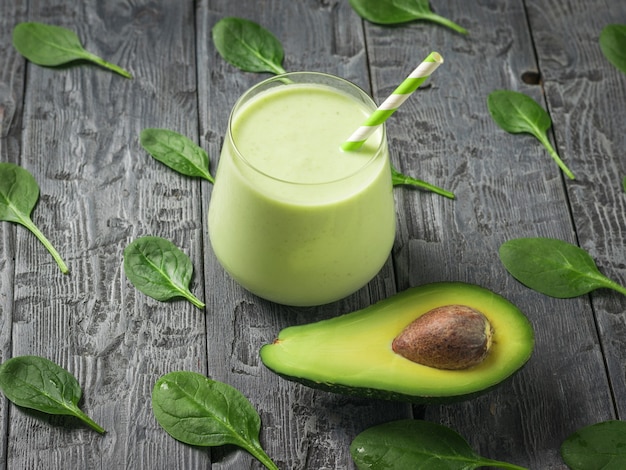 Fresh smoothie in a glass glass with avocado on a wooden table with spinach leaves. Fitness product. Dietary sports nutrition.