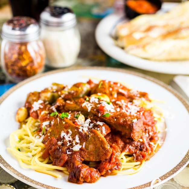Свежие спагетти с колбасой, перцем и луком в итальянском ресторане.