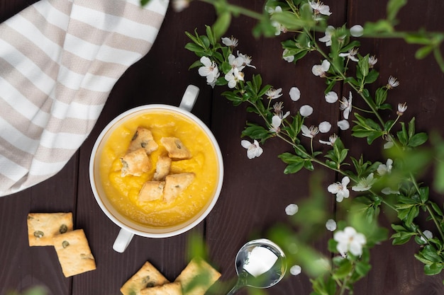 Fresh spicy organic creamy pumpkin soup in white bowl on wooden table with bread crackers Top view