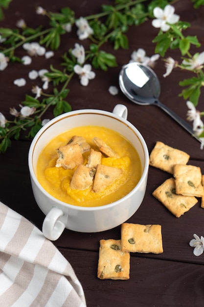 Fresh spicy organic creamy pumpkin soup in white bowl on wooden table with bread crackers