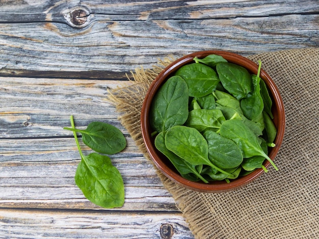 Spinaci freschi in una ciotola e tela di sacco riciclata sulla vecchia tavola di legno